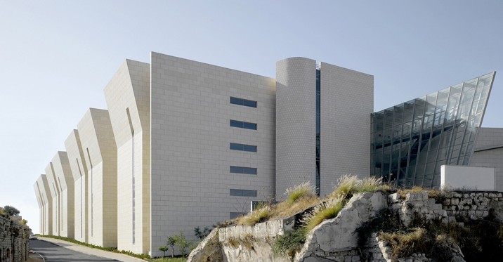 Haifa Supreme Court — long stone elevation stepping down the hillside, with faceted fin bays and the glazed prow of the courtroom wing