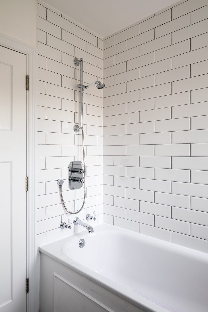 Bathroom with white metro tiles, exposed thermostatic shower fittings, and traditional cross-head taps over the bath