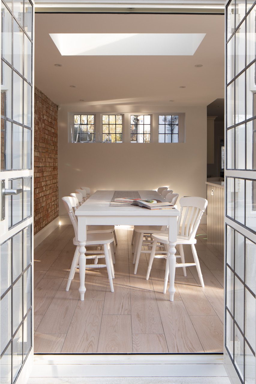 Dining room extension viewed through open glazed French doors, with exposed brick wall and rooflight above
