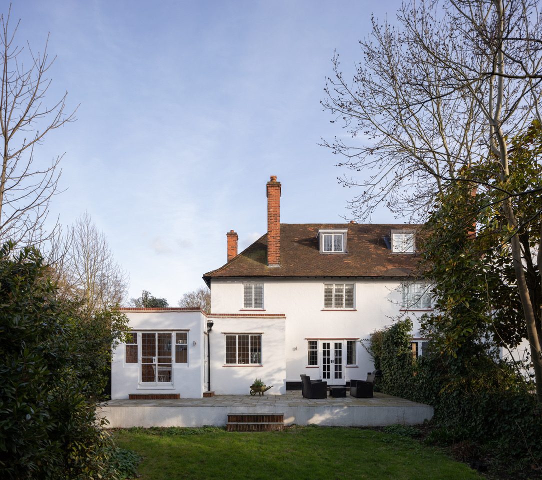 Daytime rear exterior of the white rendered house with terracotta roof, chimneys, and garden terrace seating