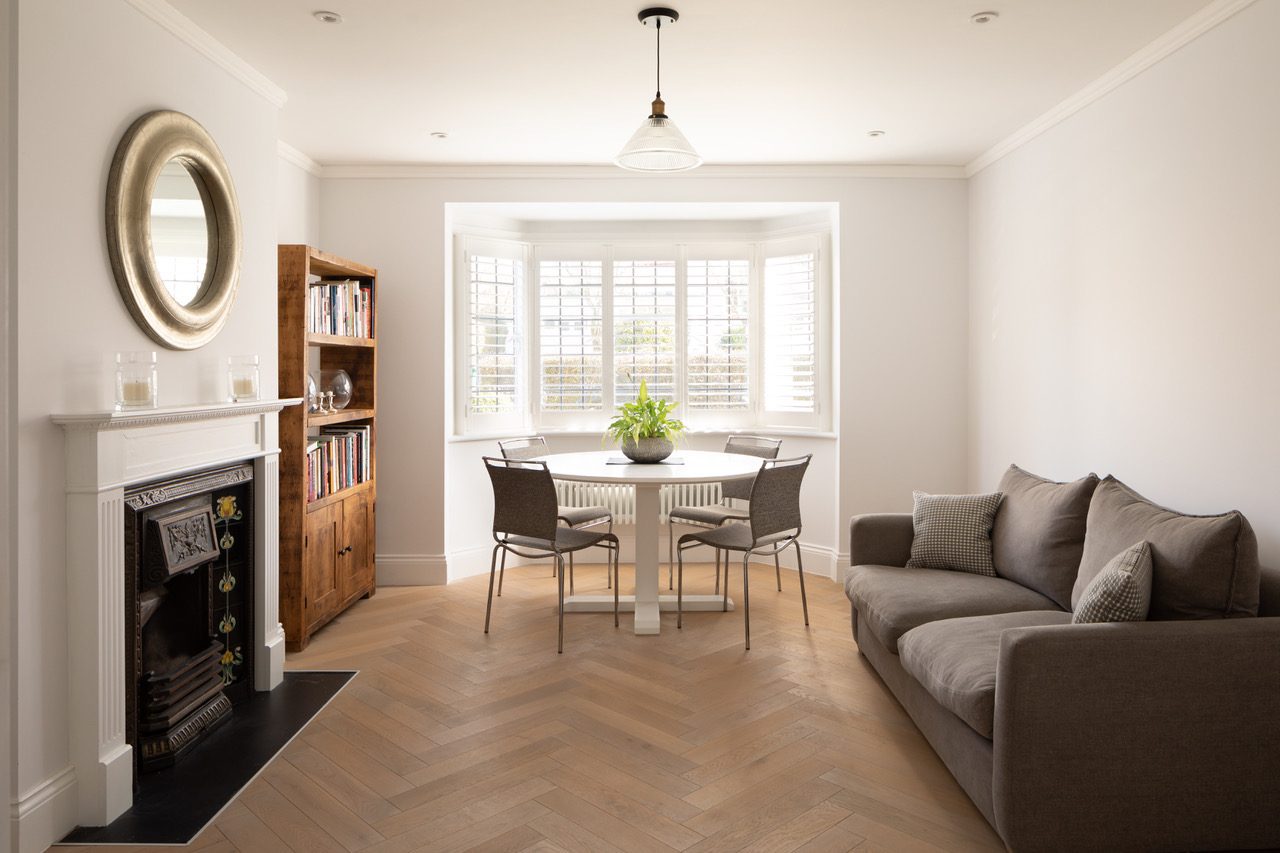 Sitting room with herringbone flooring, period fireplace, bay window seating area, and built-in bookcase