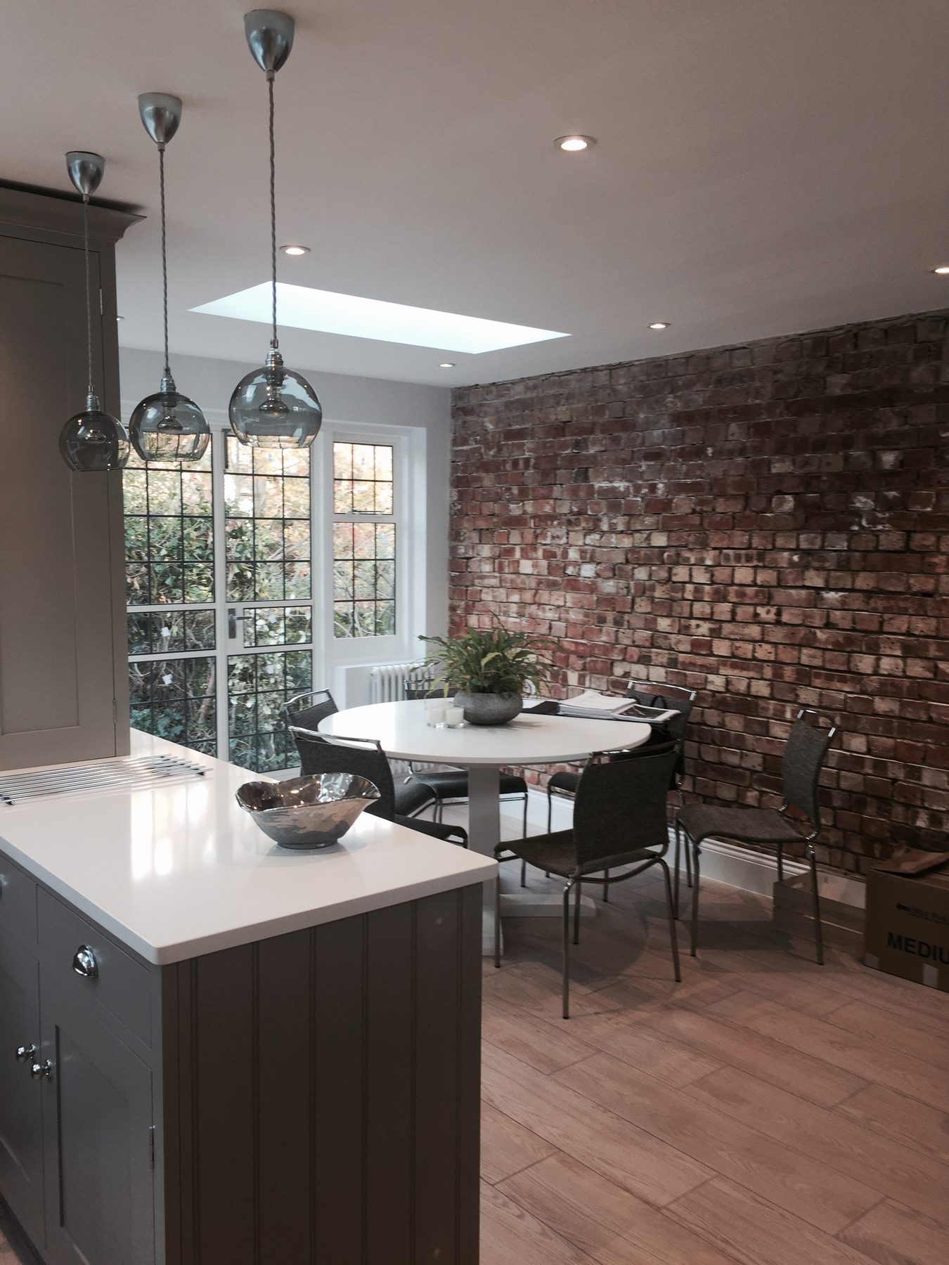 Kitchen extension with exposed brick feature wall, round dining table, and glass pendant lighting over the island