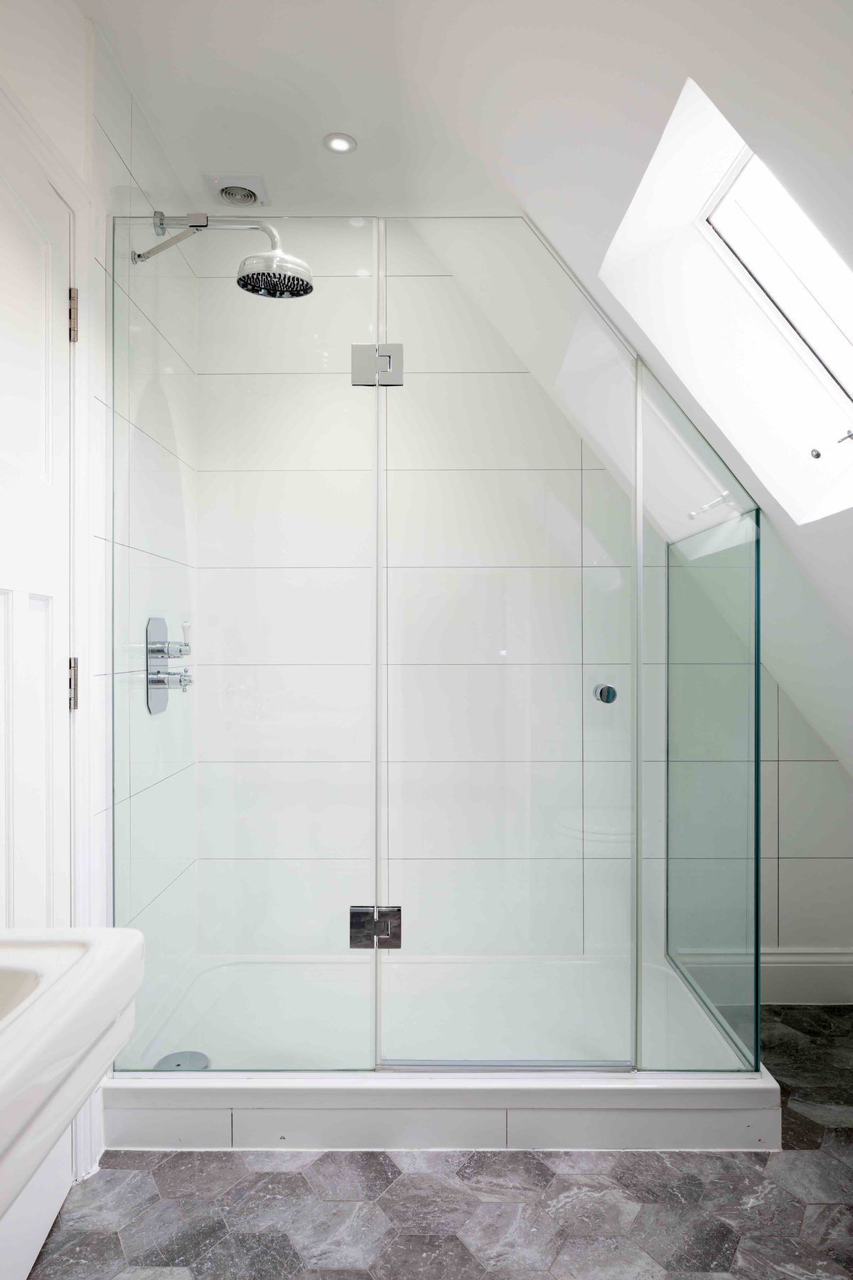 Loft en-suite shower room with frameless glass enclosure fitted beneath the sloped roofline and skylight