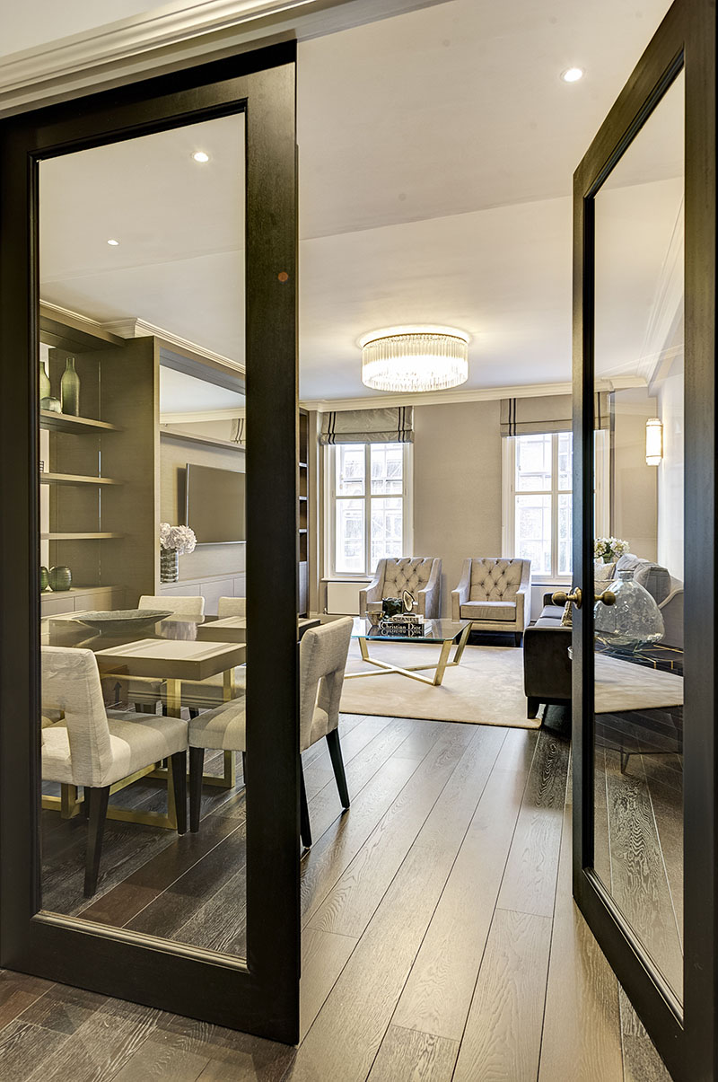 Black-framed glass pivot doors opening from the hallway into the dining and living room