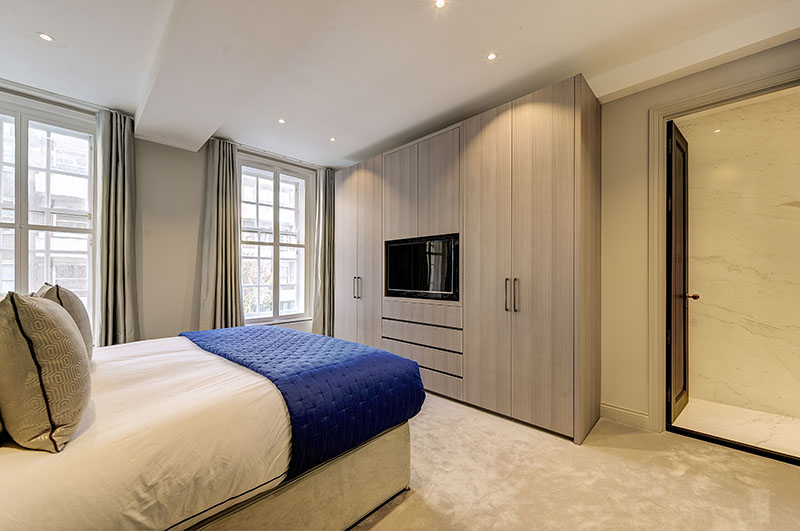 Master bedroom with full-height fitted wardrobes, integrated TV unit and navy quilted throw