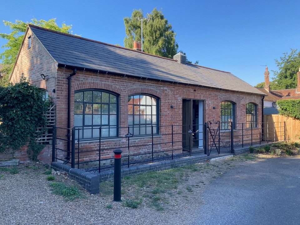 Front elevation of The Old Forge in summer, arched steel windows and railings to the village lane