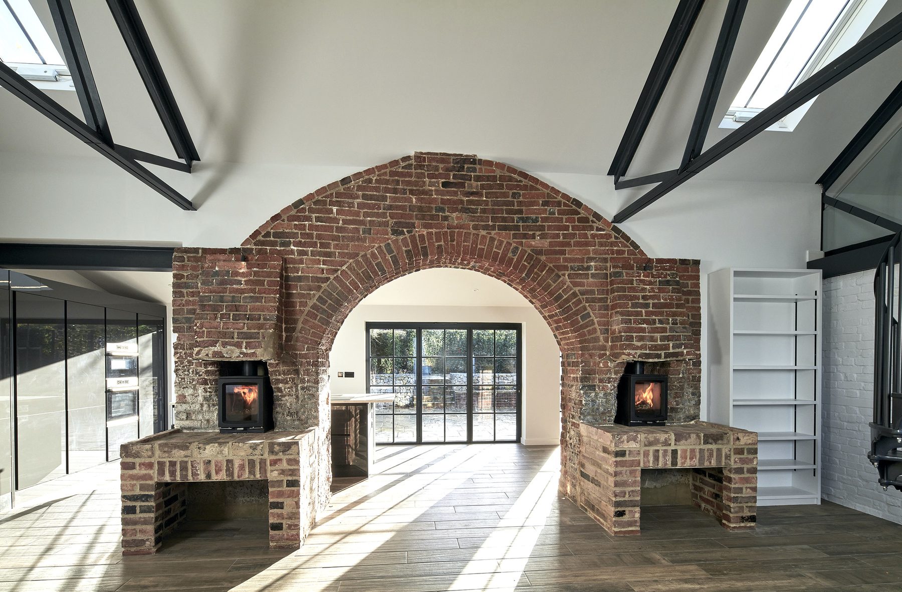 The retained forge arch in reclaimed brick, with twin wood-burning stoves set into brick hearth benches either side