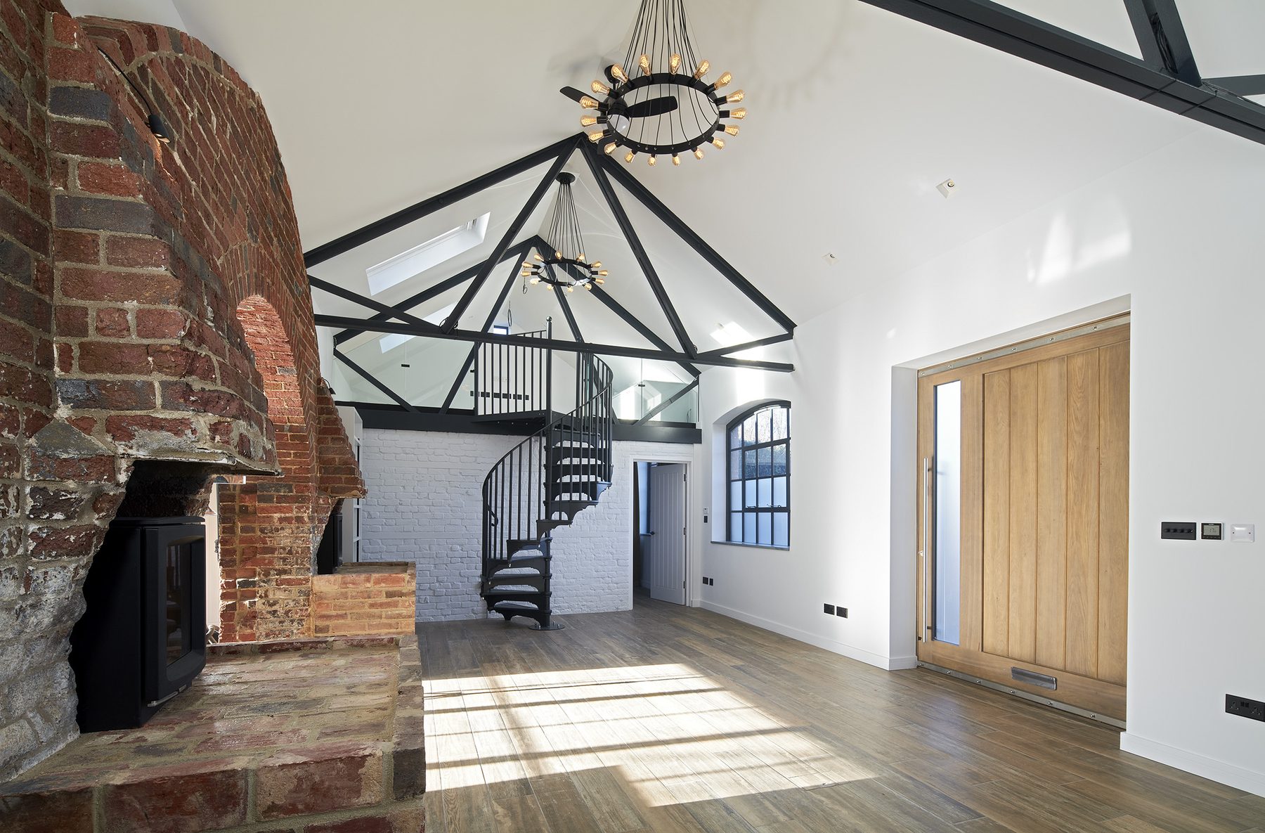 Entrance hall with oak front door, painted brick wall and spiral staircase rising to the mezzanine gallery