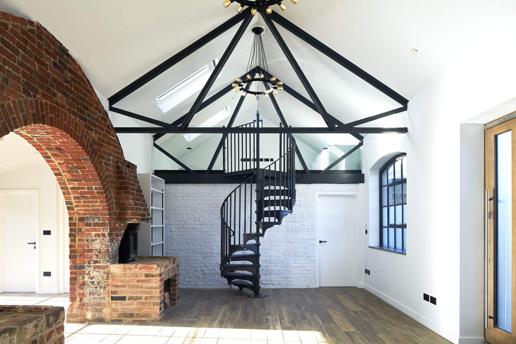 Double-height living space with exposed black steel roof trusses, rooflights and ring chandeliers