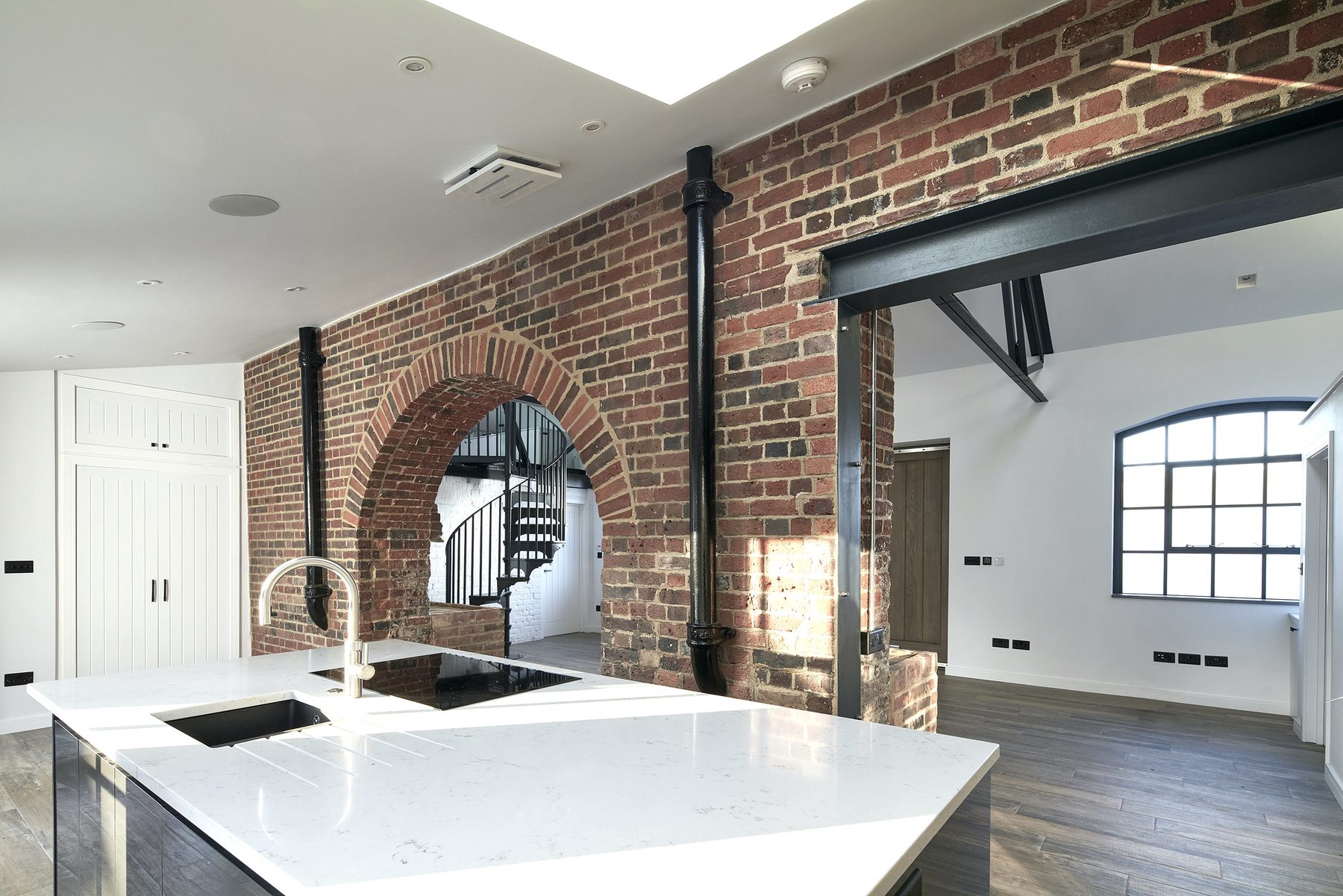 Kitchen island in white quartz set against the salvaged brick archway framing the route to the entrance hall