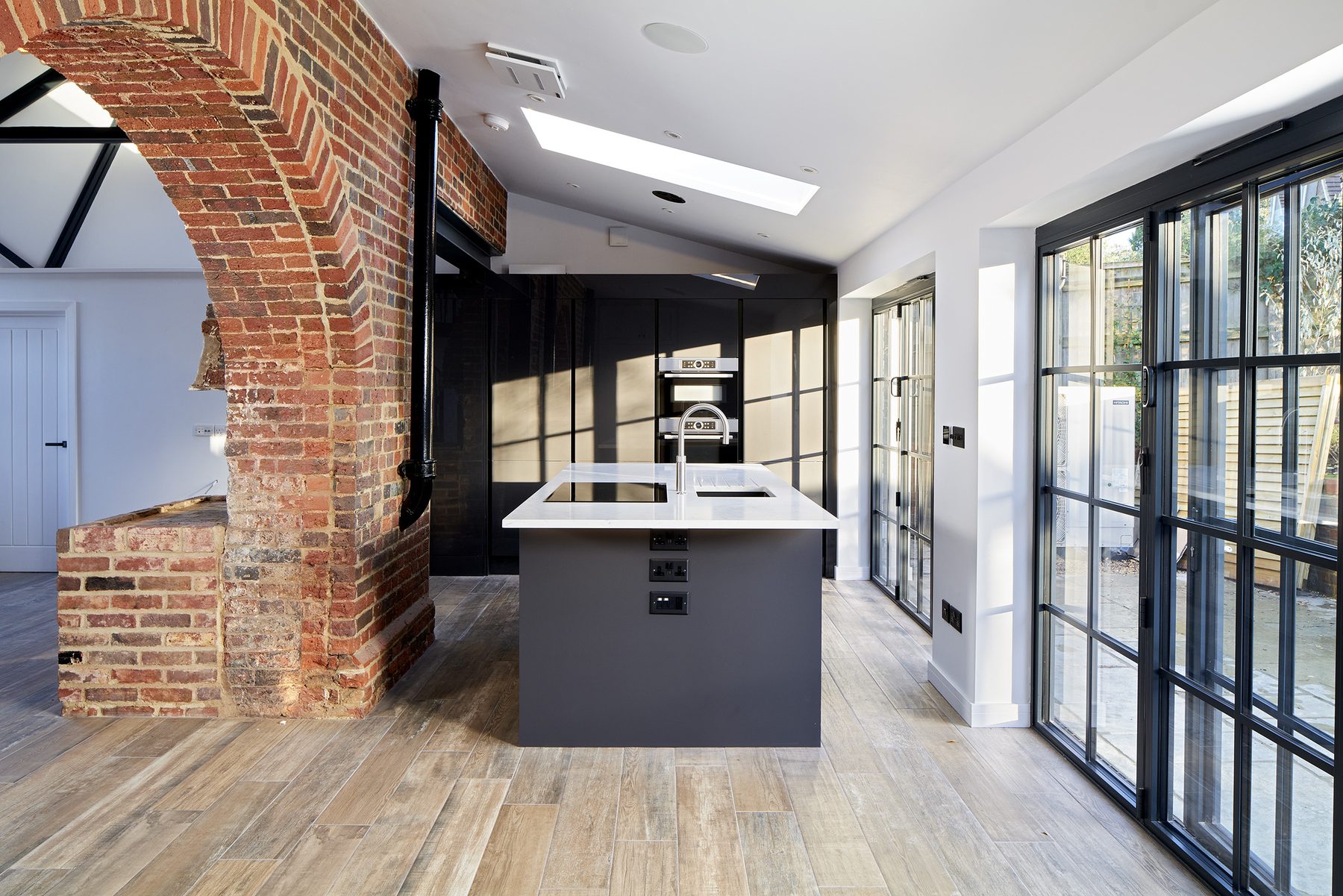 Kitchen extension with dark cabinetry, integrated ovens and steel-framed glazed doors to the terrace