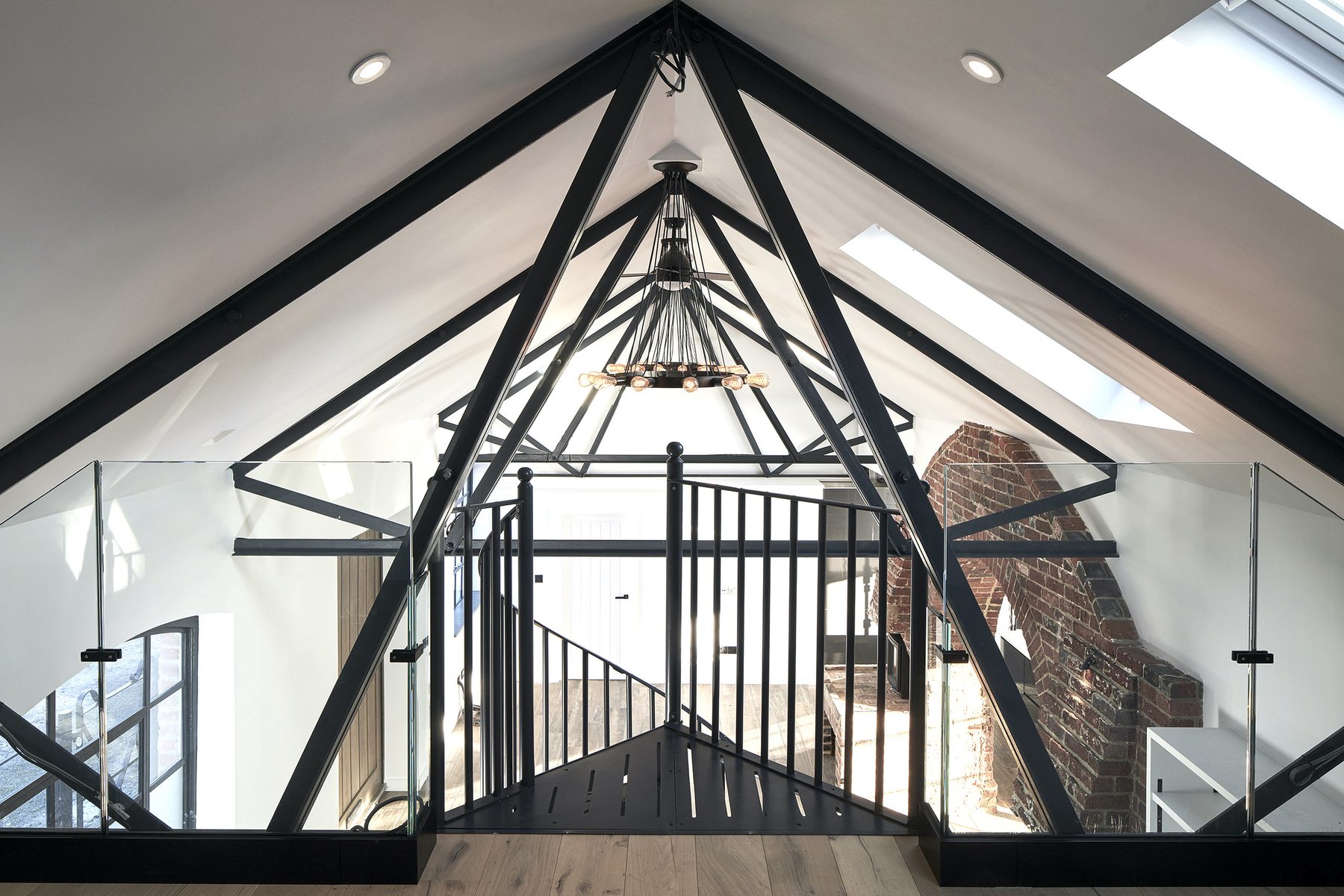 Mezzanine gallery beneath the steel roof trusses, with frameless glass balustrade and oak flooring