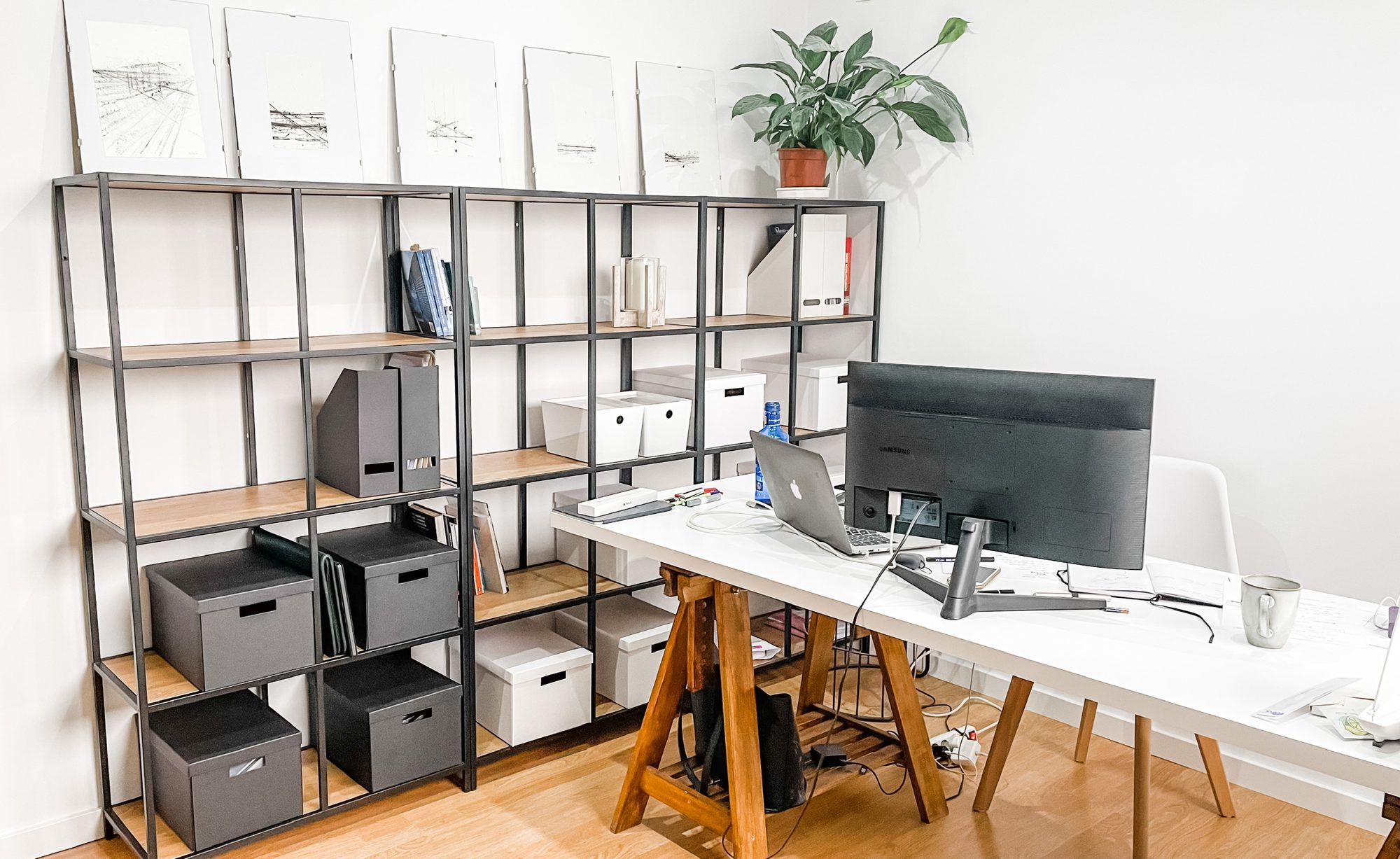 The Studio Basheva office: a long trestle drawing desk beside open steel-and-oak shelving, with framed architectural drawings ranged along the wall above